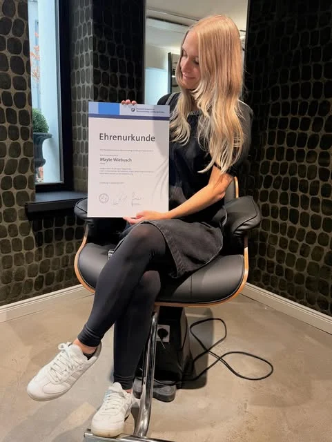 Mayte im Salon mit ihrer Ehrenurkunde